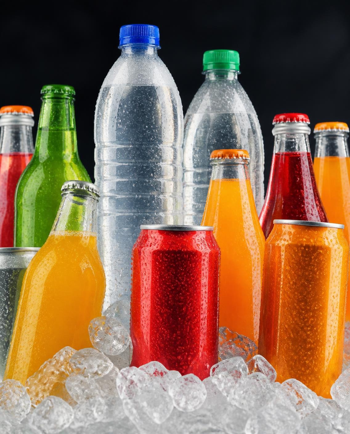 Ice-cold glass and plastic bottles of water, juice and soft drinks with cans, chilled on crushed ice